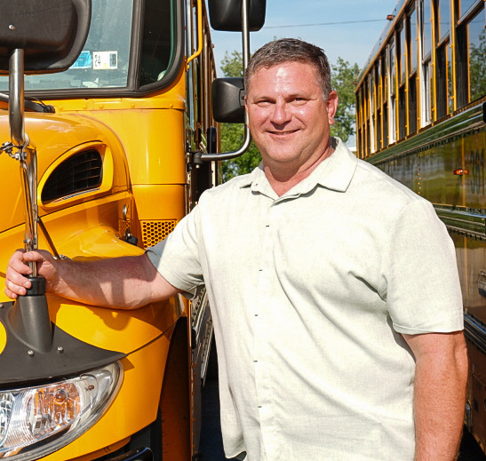 Mike Massaro, President of Krise Transportation standing beside a yellow bus.